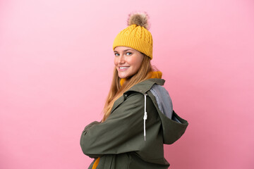 Young blonde woman wearing winter jacket isolated on pink background with arms crossed and looking forward