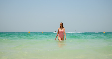 Fototapeta na wymiar Tourist woman in swimsuit leave the sea after swimming on Jumeirah beach.