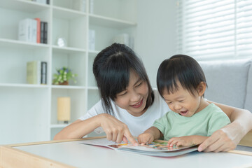 Fototapeta na wymiar Happy Asian mother relax and read book with baby time together at home. parent sit on sofa with daughter and reading a story. learn development, childcare, laughing, education, storytelling, practice.