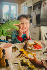 Uśmiechnięty chłopiec przy stole w kuchni, śniadanie w domu. Dinozaury na stole, zabawa przy śniadaniu. © malgo_walko