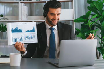 Business man wearing headphone present financial data or BI paper via laptop during online meeting....