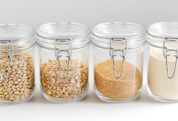 food storage, culinary and storage concept - close up of jars with oat flakes, semolina, couscous and beans on white background
