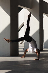 an acrobat guy, standing on one arm, in a white T-shirt and black pants, without shoes, in a...