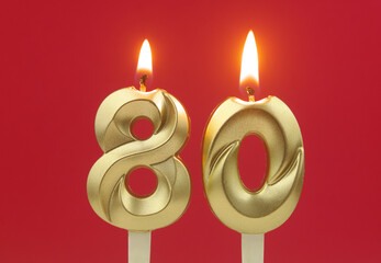 Golden birthday candles burning and melting on red background, number 80