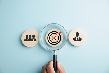 In the stock photo, a magnifier glass zooms in on a target icon surrounded by businessmen,...
