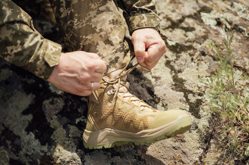 Ukrainian military man tying shoelaces. Summer option. Uniform with pixel pattern