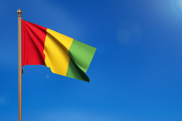 Guinea. Flag blown by the wind with blue sky in the background.