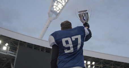 American football player rising a trophy during a award ceremony on a stadium. Winning the...