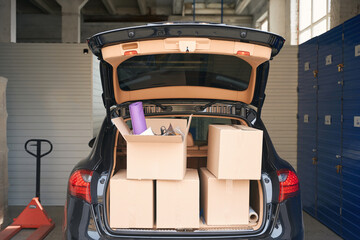 Cropped photo of cardboard boxes with things in the trunk of car into warehouse