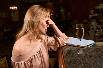 Disappointed lady sitting alone with glass of alcohol in the bar