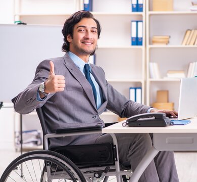 Young handsome employee in wheelchair at the office