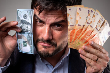 Hombre triste por la devaluación sosteniendo pesos argentinos y un billete de 100 dolares - obrazy, fototapety, plakaty