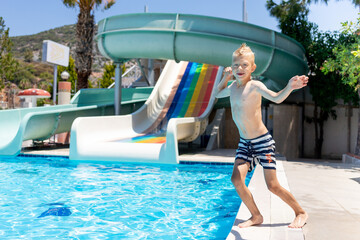 happy baby boy jumps into the pool with water slides and smiles, the concept of a summer vacation at the sea and holidays