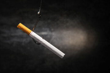 Cigarette hanging on hook against dark background. Stop smoking concept
