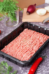 Plastic package with fresh minced meat and vegetables on grey grunge background