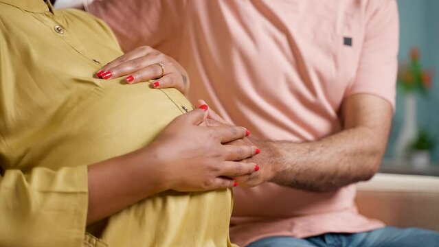Close up shot of husband holding feeling by touching the belly of pregnant wife at home - concept of parenthood, affectionate and expecting.