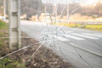 A glass window of a car punched by an angry people who hits a punch, a blurry background of a street with road and grass on a summer day