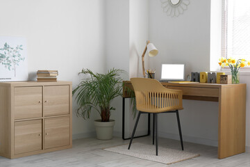Comfortable workplace with modern laptop and narcissus flowers on table in room