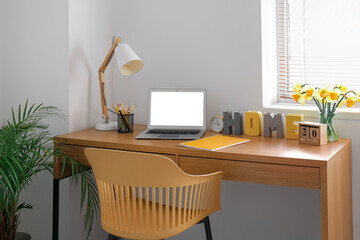 Comfortable workplace with modern laptop and narcissus flowers on table in room