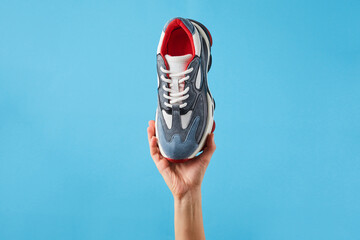 Hand holds a new comfortable sports shoe. Sneakers for sports on a blue background. Shoes for...