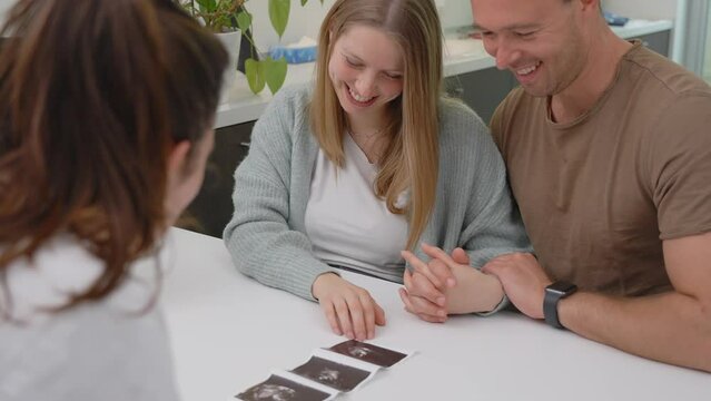 Doctor in clinic room showing ultrasound scan of baby to young couple - Gynecology consultation, pregnancy and artificial insemination concept