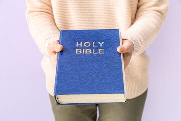 Woman holding Holy Bible on lilac background