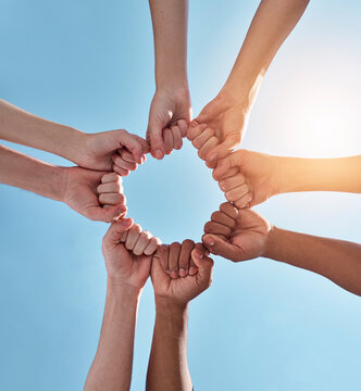 Diversity, fist pump and hands in a circle together for unity, collaboration and teamwork. Solidarity, empowerment and closeup of a group of multiracial people in a round shape by a sky background.