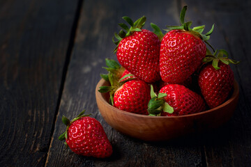 Berries of red strawberries in a wooden bowl on a dark wooden table