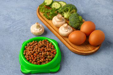 Bowl with dry pet food and natural products on color background, closeup