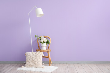 Vase with lilac flowers on chair, pillow and lamp in room