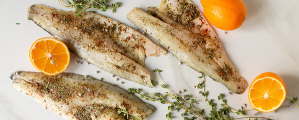 sea bass fillet with herb marinade, lemons and thyme on a light table
