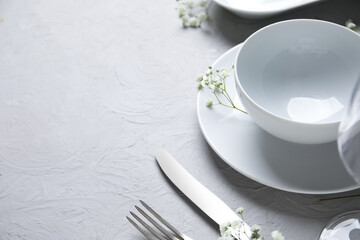 Plates with silver cutlery, flowers and glass on grunge grey background