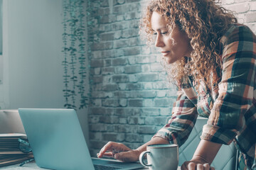 One pretty adult woman writing message on computer at home on the table alone. Side view of female...