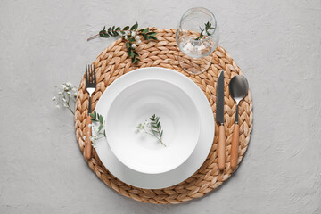 Wicker mat with plates, cutlery and glass on grunge grey background