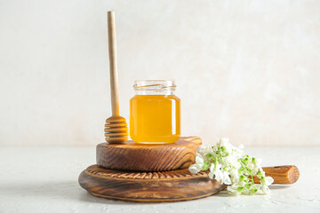 Jar of honey with flowers of acacia and dipper on light background