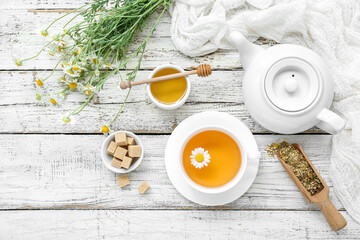 Cup of hot chamomile tea, teapot and honey on light wooden background