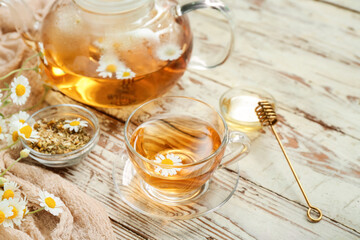 Cup of hot chamomile tea on light wooden background