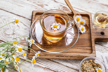 Cup of hot chamomile tea on light wooden background