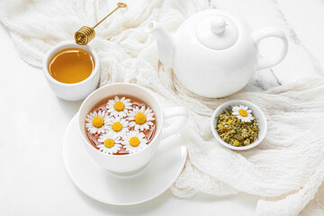 Cup of hot chamomile tea, teapot and honey on white marble background