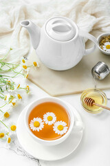 Cup of hot chamomile tea, teapot and honey on white marble background