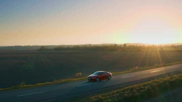 Aerial tracking shot of a red Audi automobile driving on a rural asphalt road.
