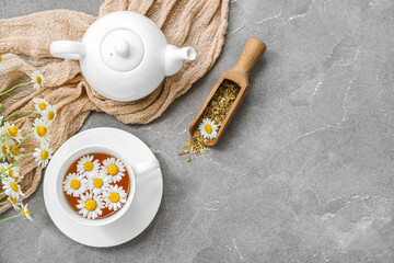 Cup of hot chamomile tea and teapot on grey background