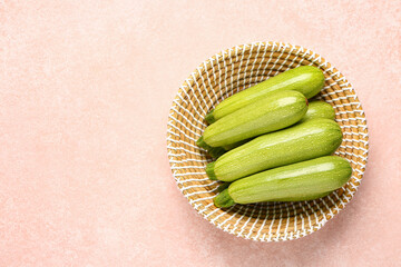 Wicker bowl with fresh green zucchini on beige background