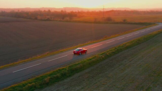 Aerial shot of a red car driving along an asphalt highway road.