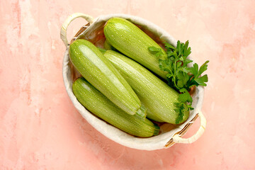 Wicker basket with fresh green zucchini  and parsley on pink background