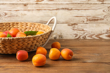 Wicker basket with fresh apricots on wooden background