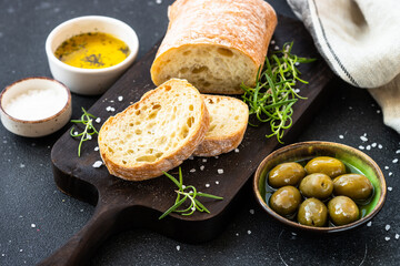 Ciabatta bread with olive oil, olives and herbs on black. Mediterranean food. Top view.