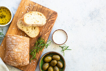 Ciabatta bread on wooden board with olive oil, olives and herbs. Top view with copy space.