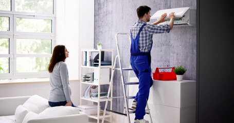 Woman And Male Technician Repairing Air Conditioner