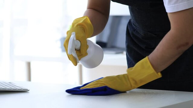 Person cleaning the room, cleaning staff is using cloth and spraying disinfectant to wipe the tables in the company office room. Cleaning staff. Maintaining cleanliness in the organization.